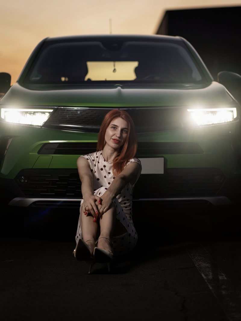 Dariia sitzend vor einem grünen Auto im Scheinwerferlicht