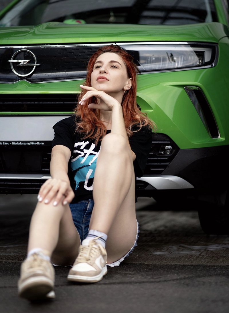 Dariia sitzend vor einem grünen Auto